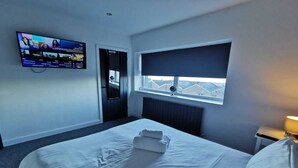 Ein Hotelzimmer mit einem Bett, einem an der Wand montierten Fernseher, einem Fenster mit Blick und einer Tür.