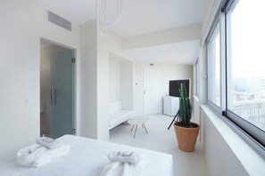 A hotel room with a bed, a potted cactus, a window with a city view, and a door leading to another room. - Athens Penthouse  (Athens)