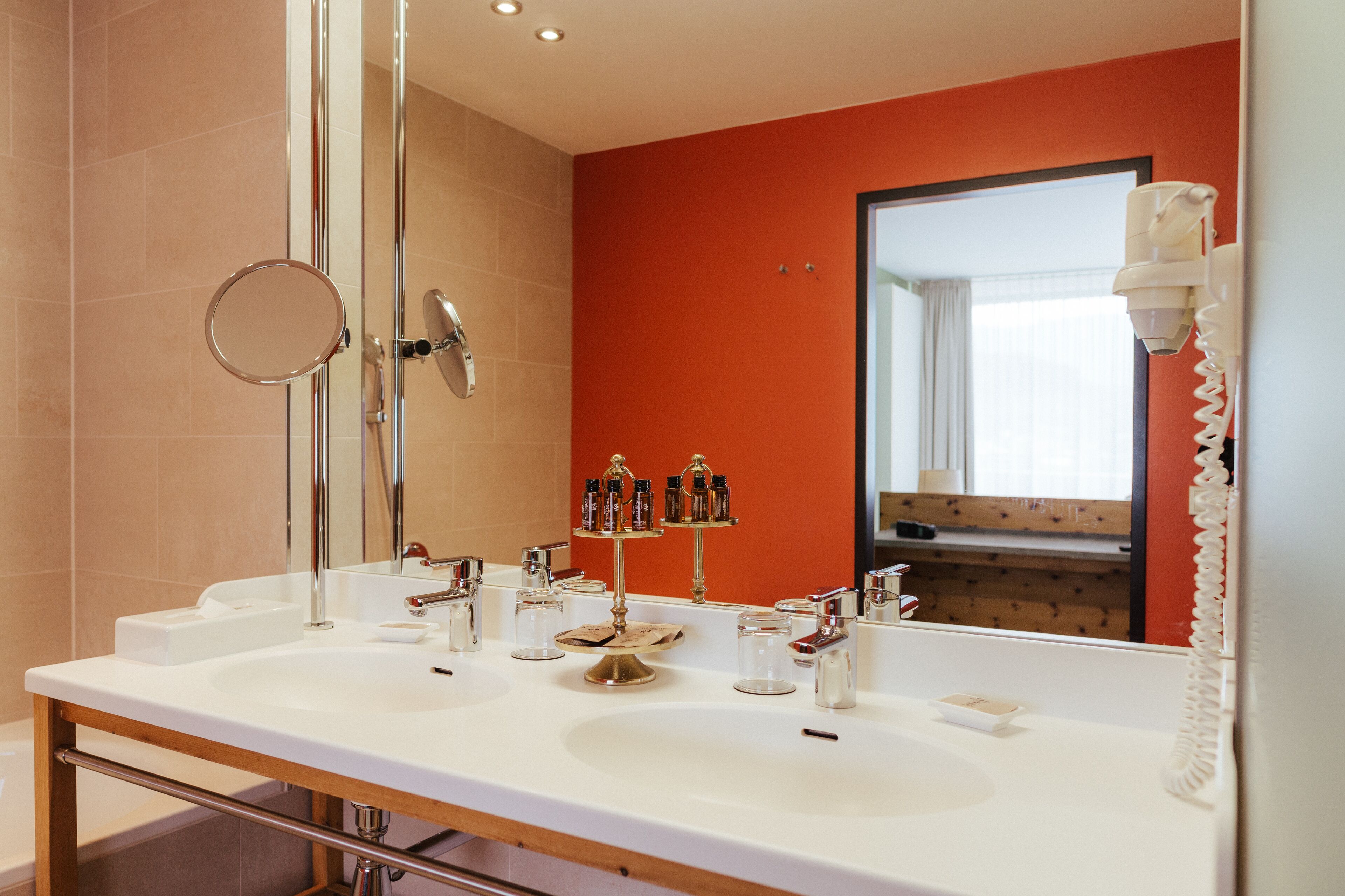 A modern bathroom with dual sinks, a large mirror, and a hairdryer mounted on the wall.