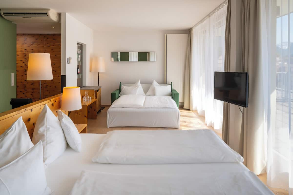 A hotel room with two beds, a TV, a desk with a lamp, and a large window with curtains.