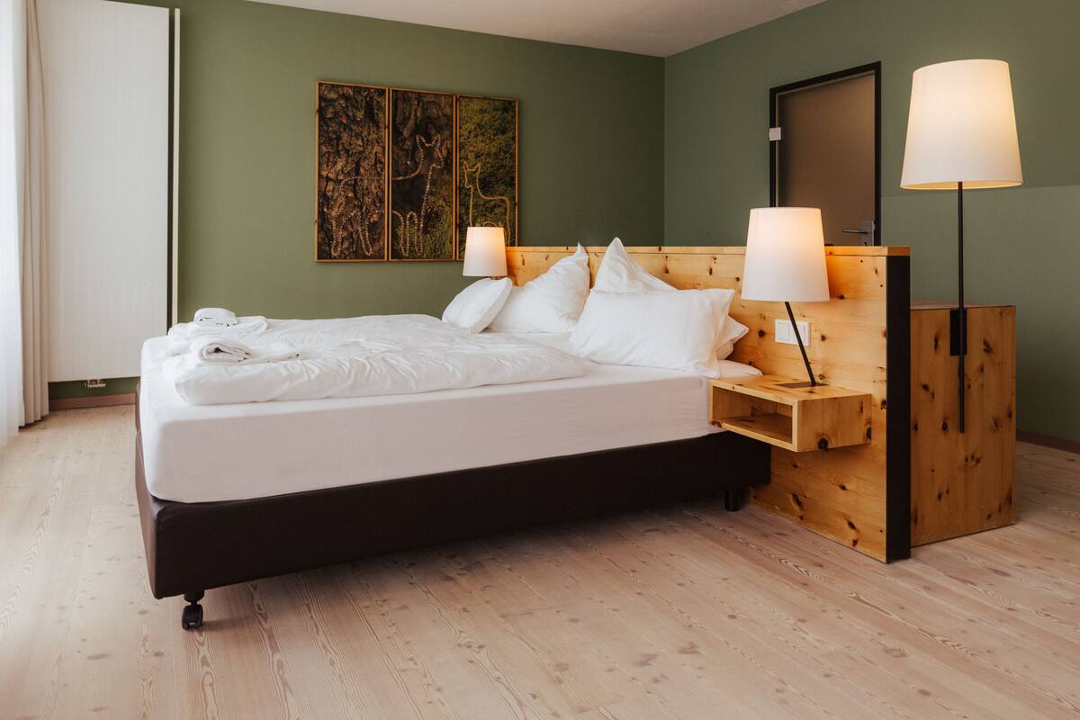 A neatly made bed with white linens, a wooden headboard, and two bedside lamps.