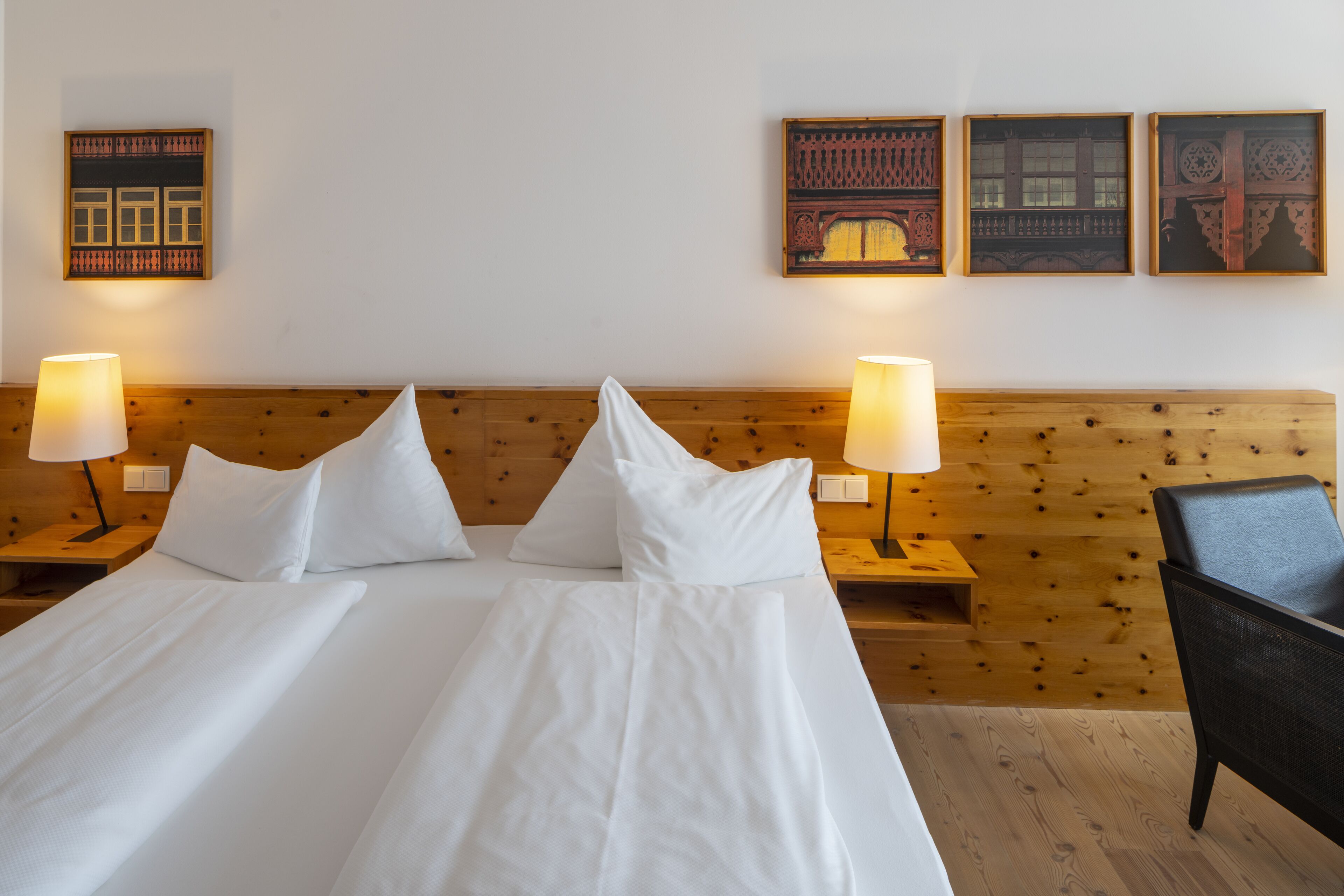 A hotel room with two beds, wooden headboard, white bedding, two bedside lamps, and three framed pictures on the wall.