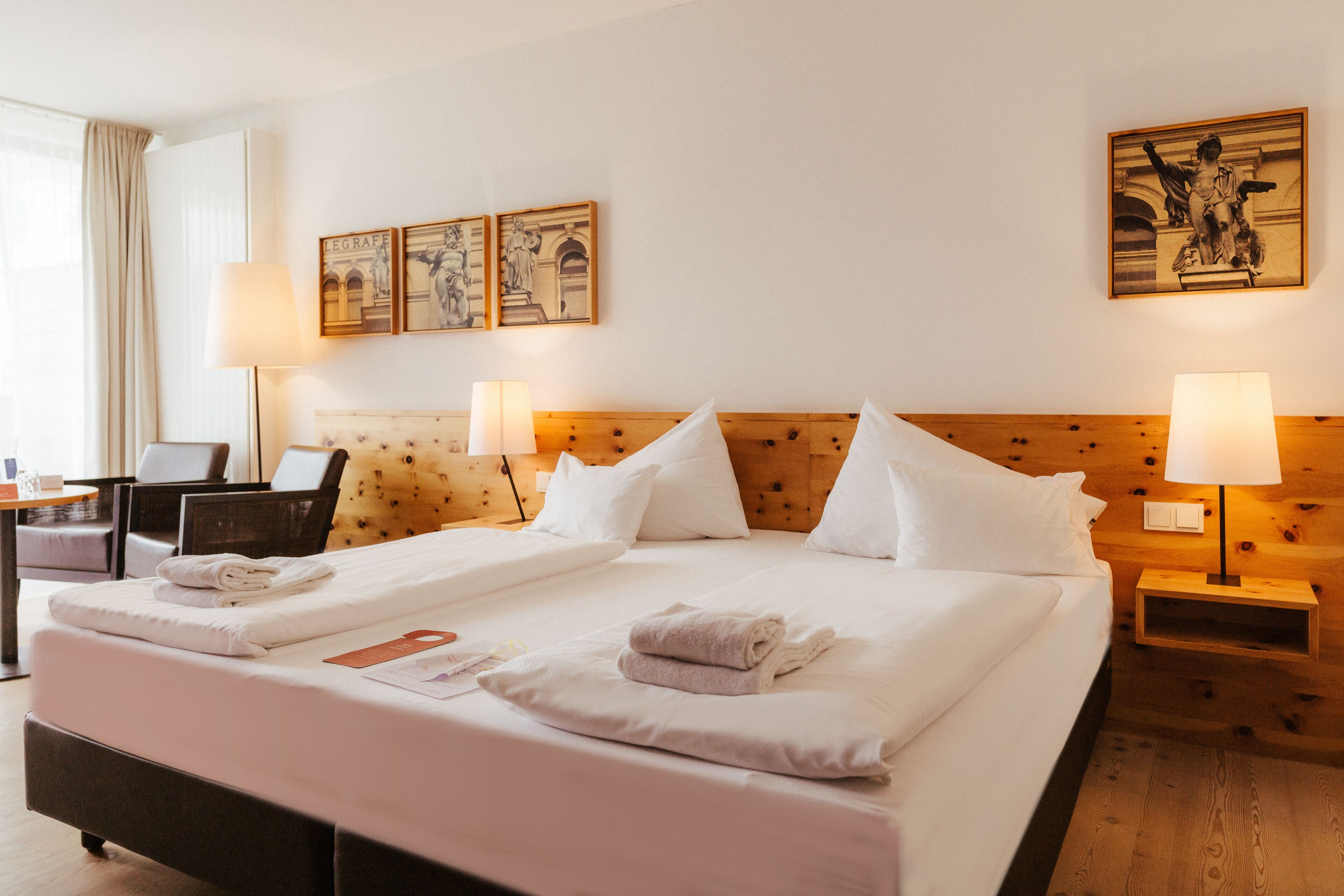 A hotel room with a large bed, two bedside tables with lamps, a wooden headboard, and artwork on the walls.