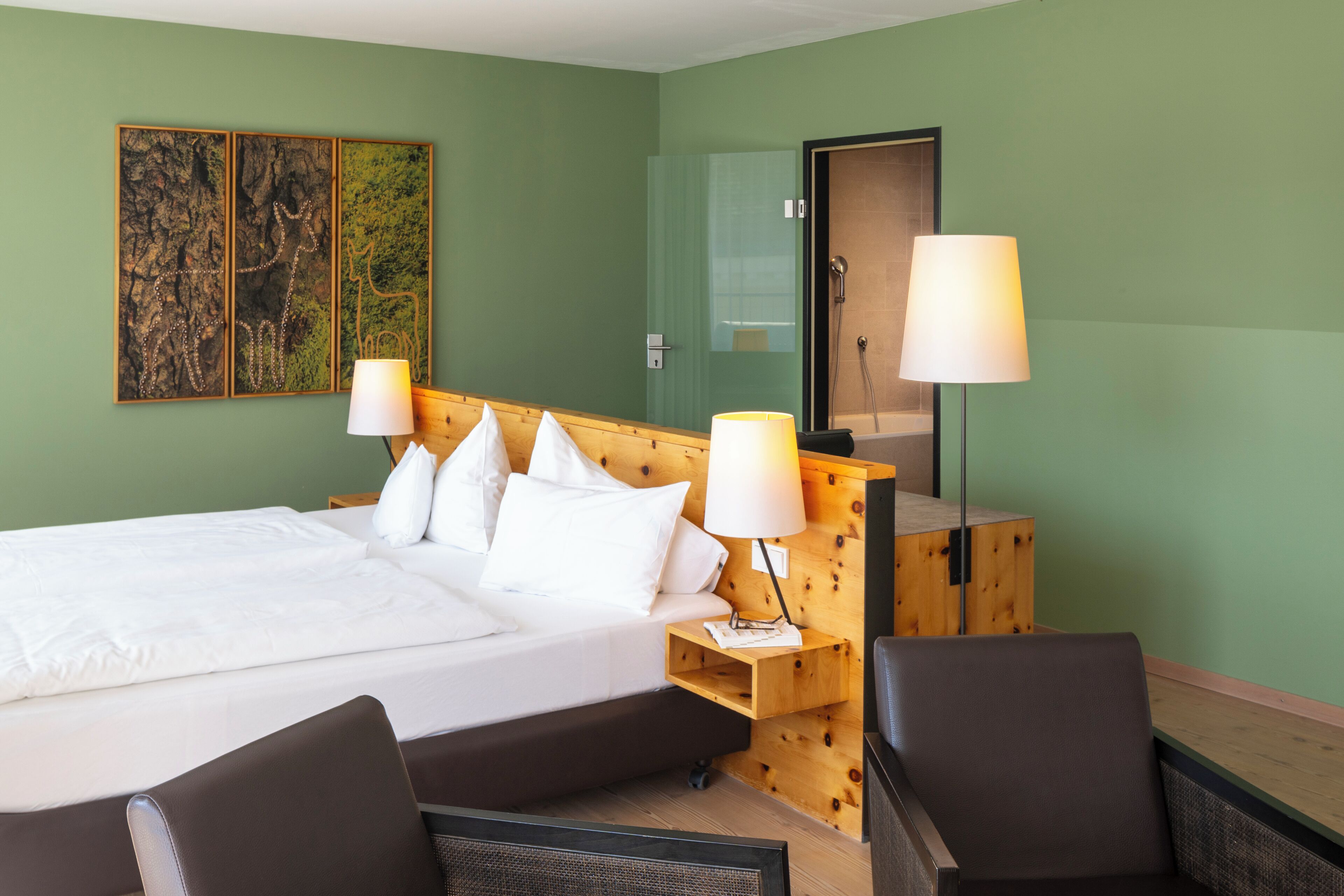 Habitación de hotel con una cama grande, dos lámparas de noche, un cabecero de madera, un espejo y una pared verde.