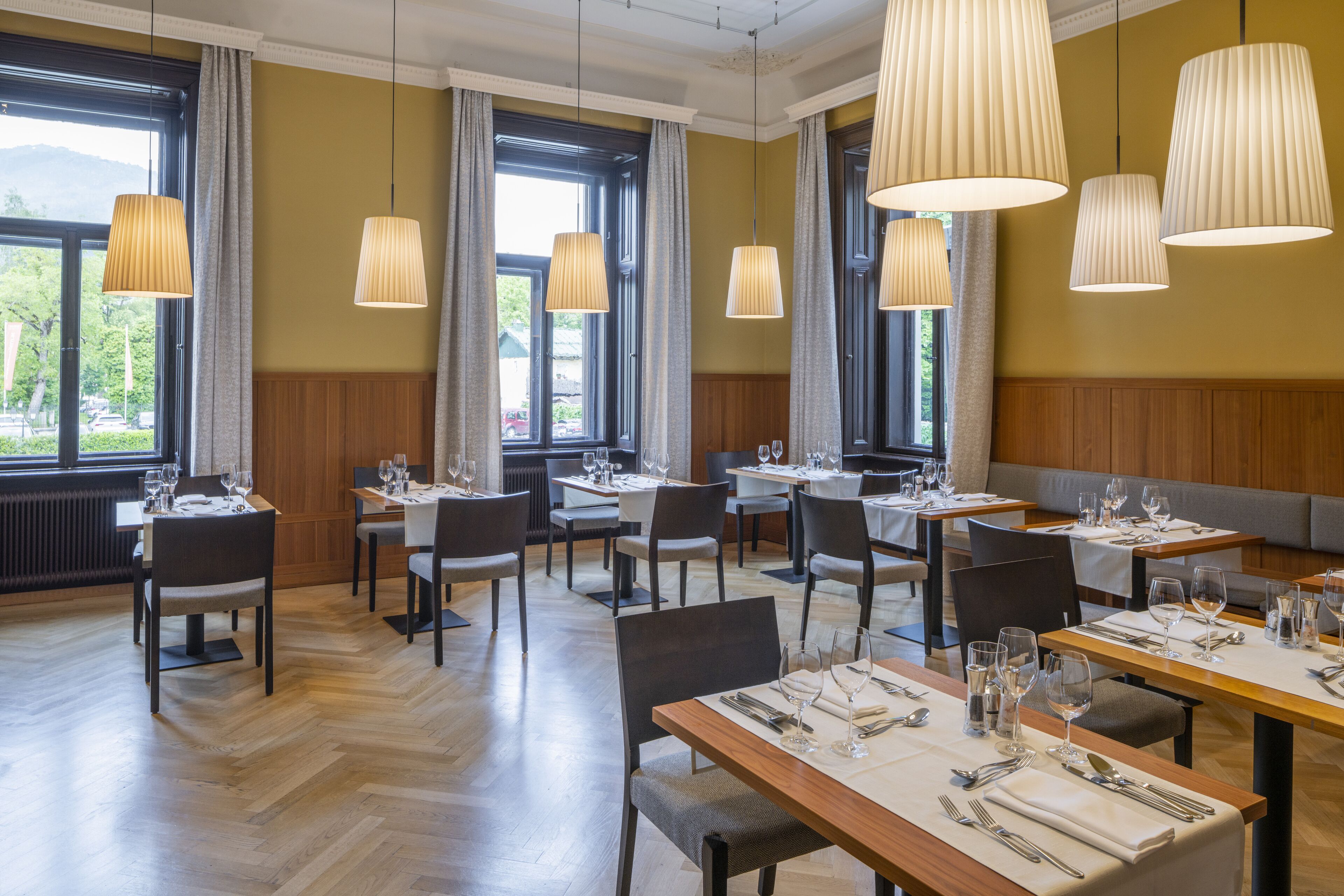 Un restaurant doté de nombreuses tables et chaises, de grandes fenêtres et de luminaires suspendus.