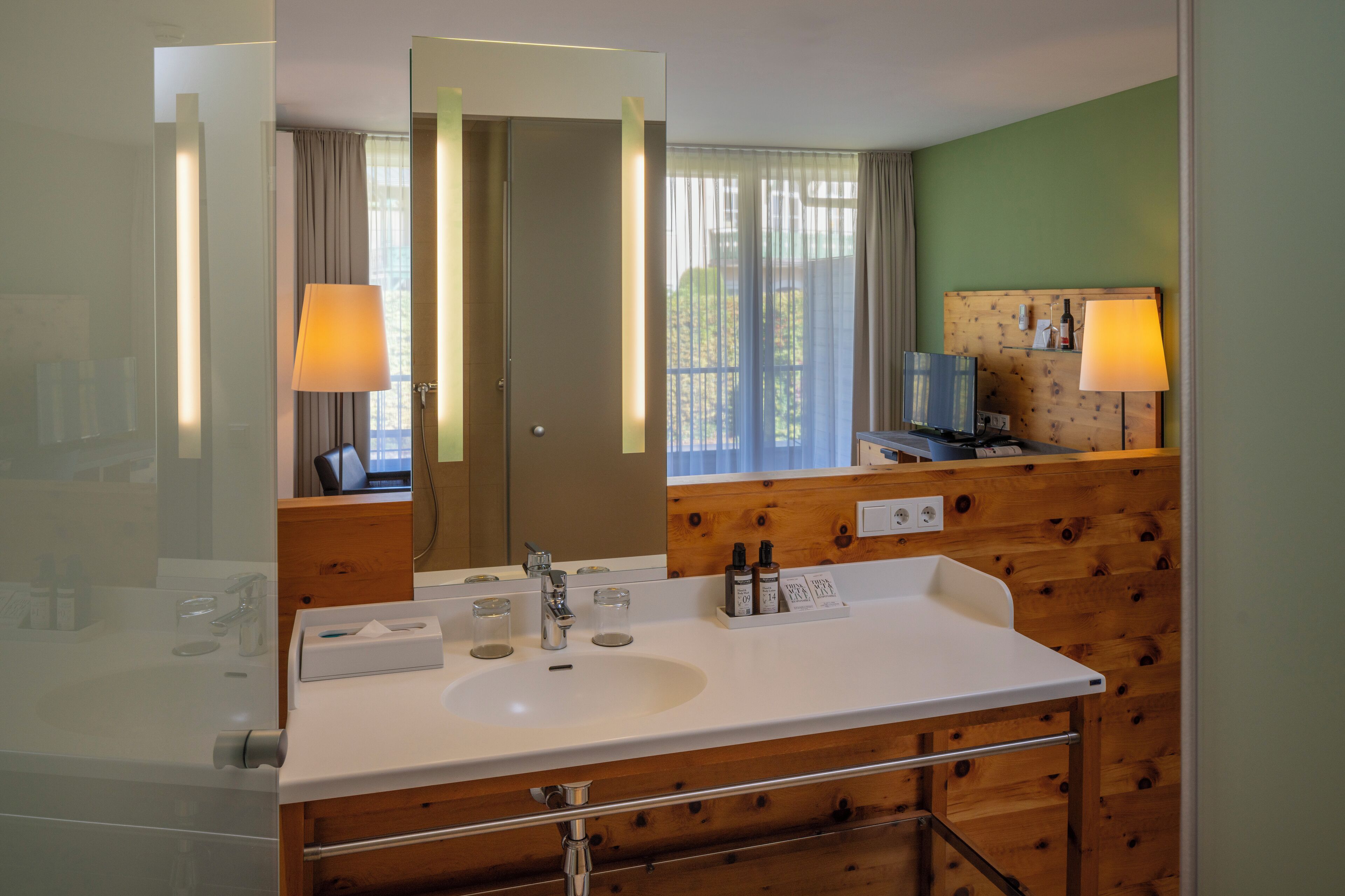 A modern bathroom with a white sink, wooden paneling, a large mirror, and two wall-mounted lamps.