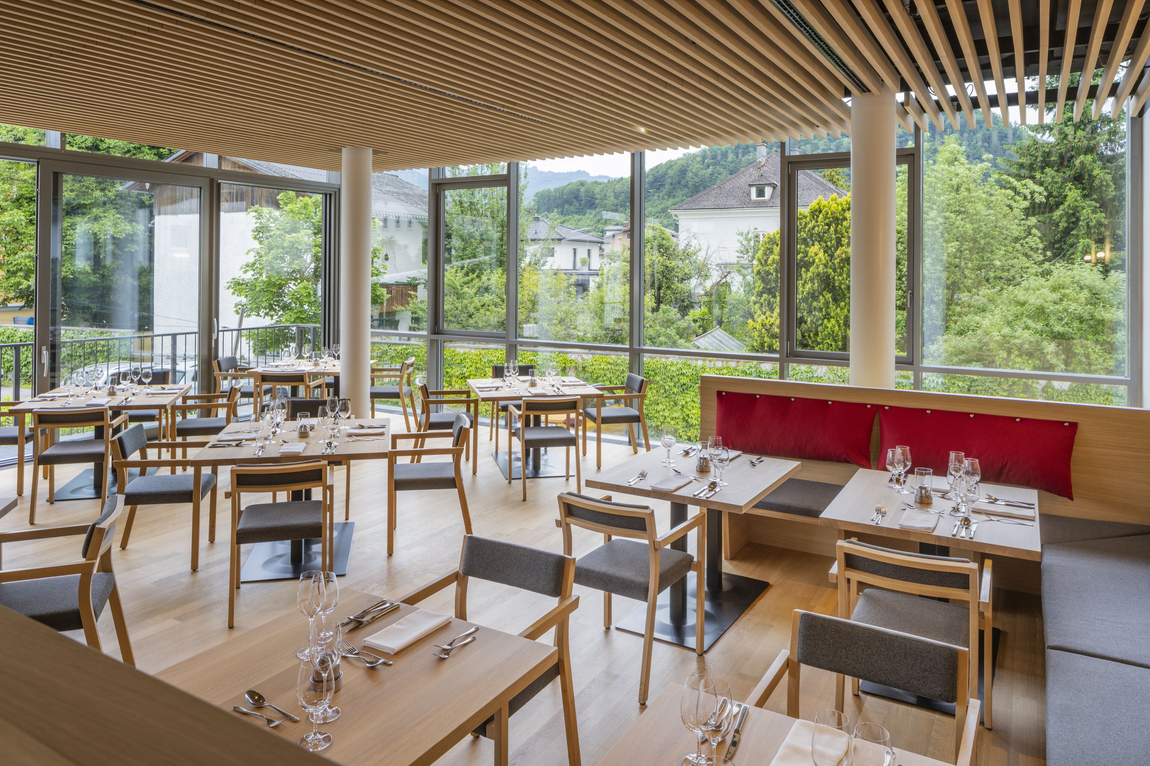 Un restaurante con amplios ventanales que ofrecen vistas a un paisaje montañoso. Las mesas están dispuestas con copas de vino y cubiertos.