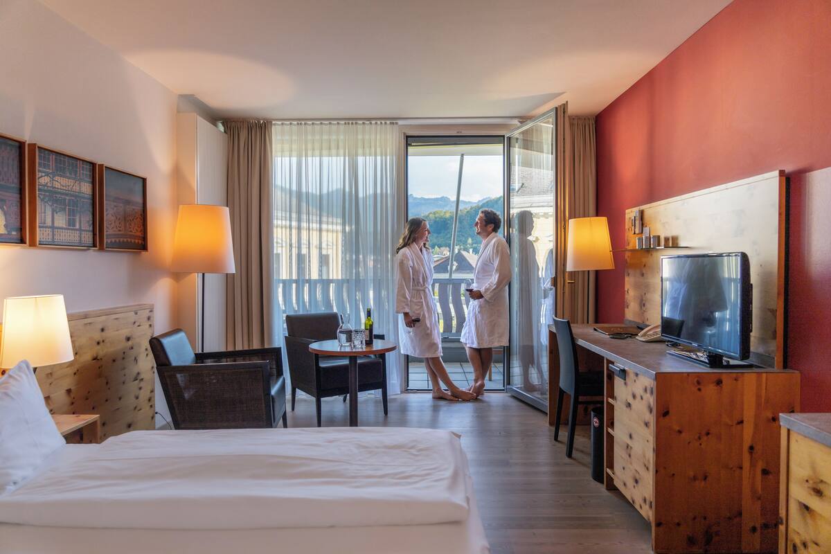 A hotel room with a bed, a desk, a television, and a view of mountains through the window.