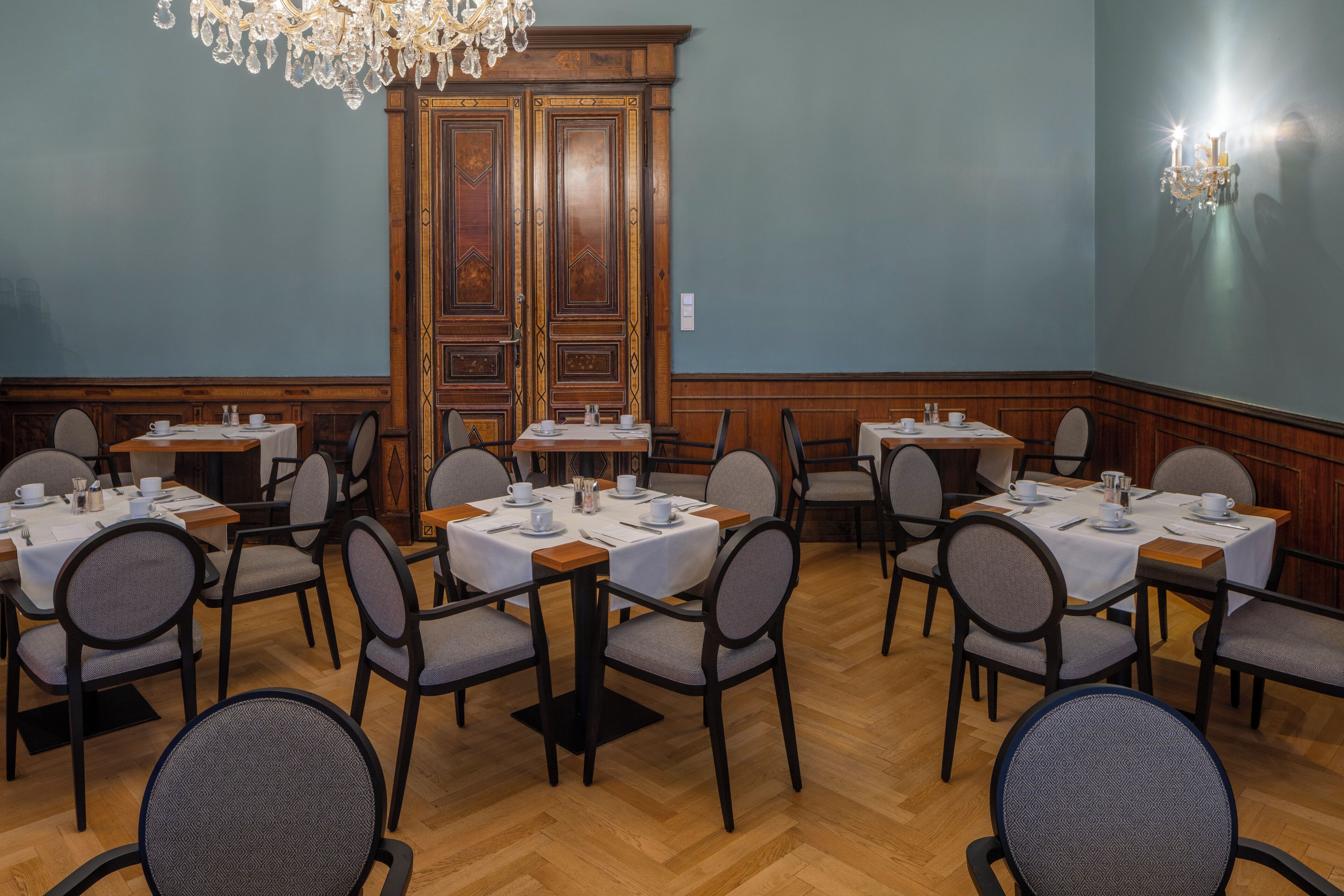 A dining area with multiple tables and chairs, wooden paneling, and a chandelier.