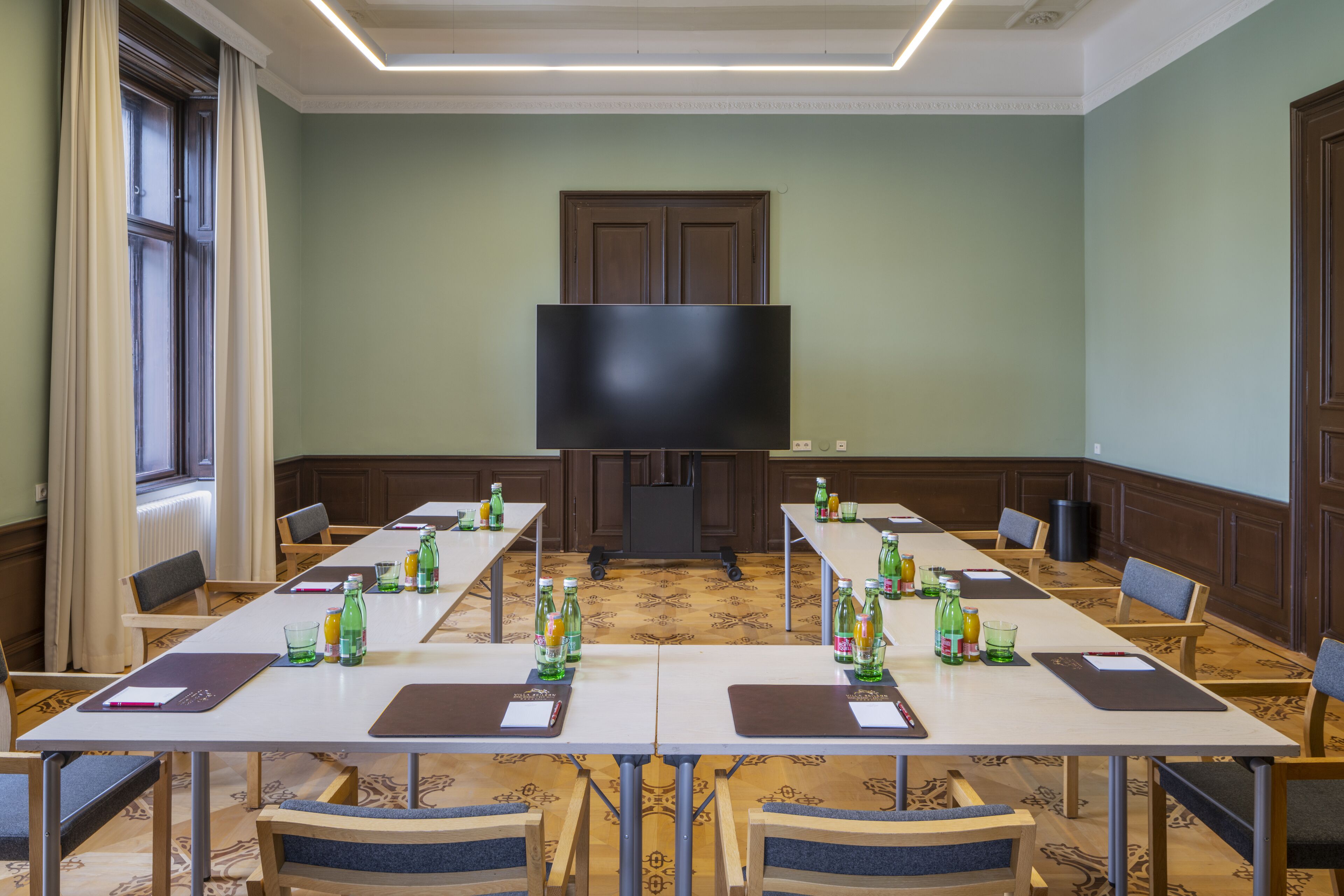 Un salón de conferencias con mesas largas, sillas y una pantalla grande al frente.