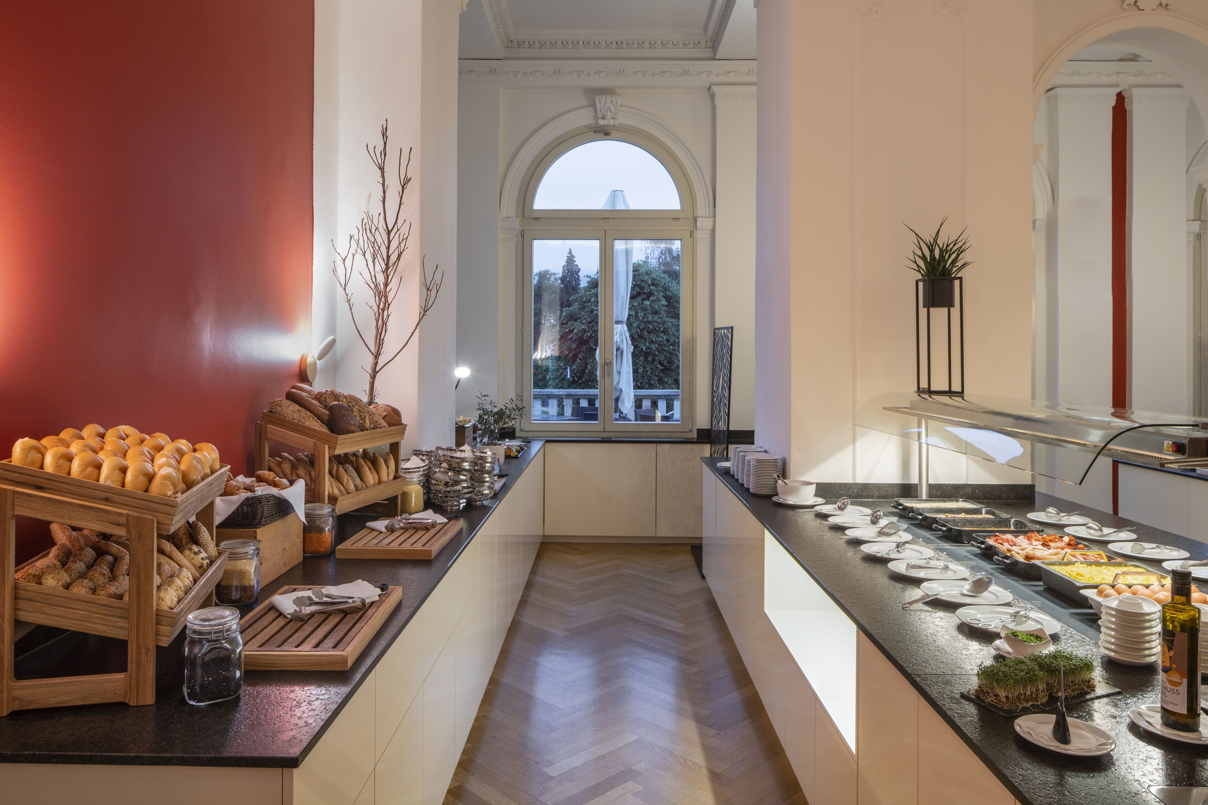 A breakfast buffet with various food items and a view of the outdoors through a large window.