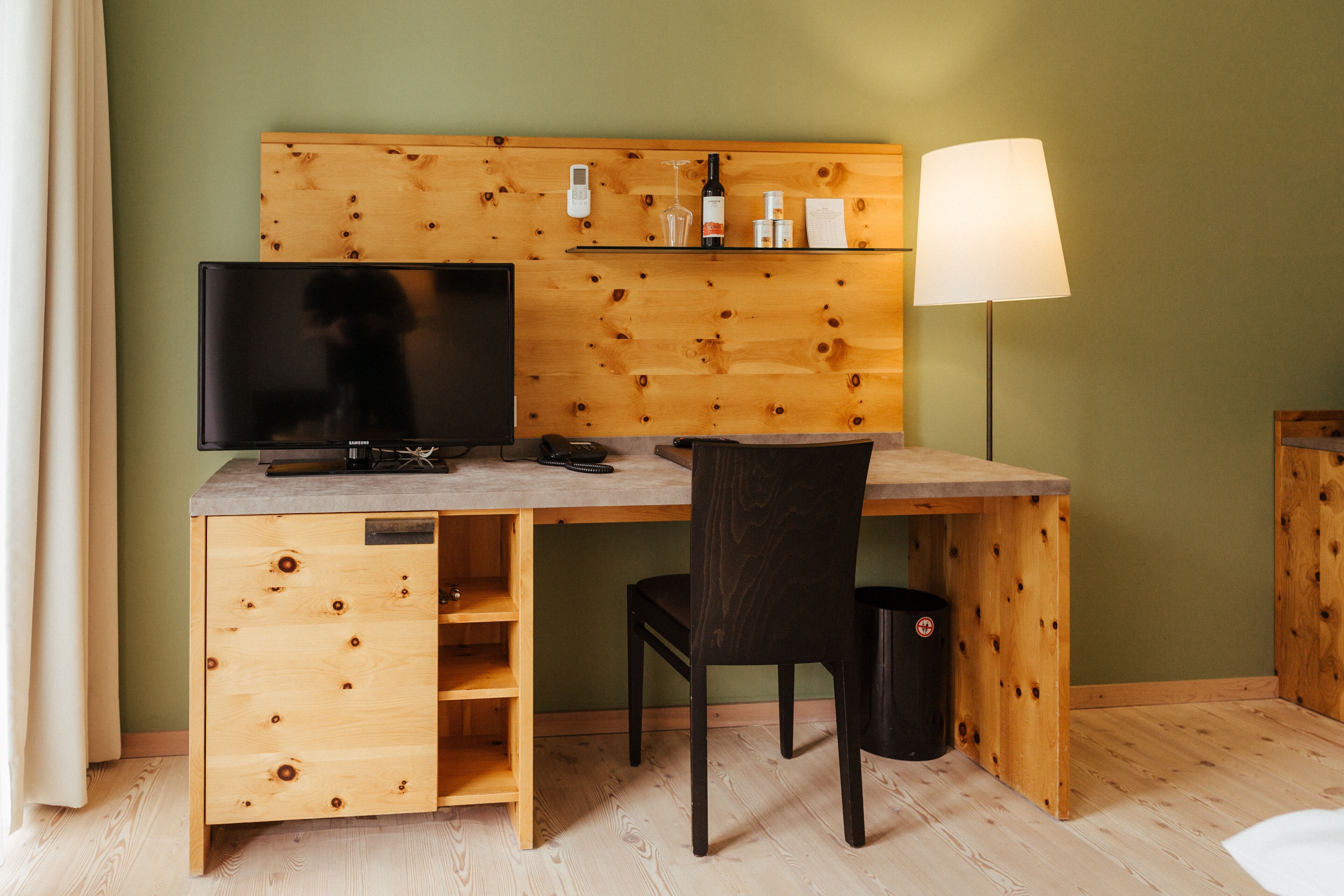 A wooden desk with a television, a lamp, and a shelf with toiletries.