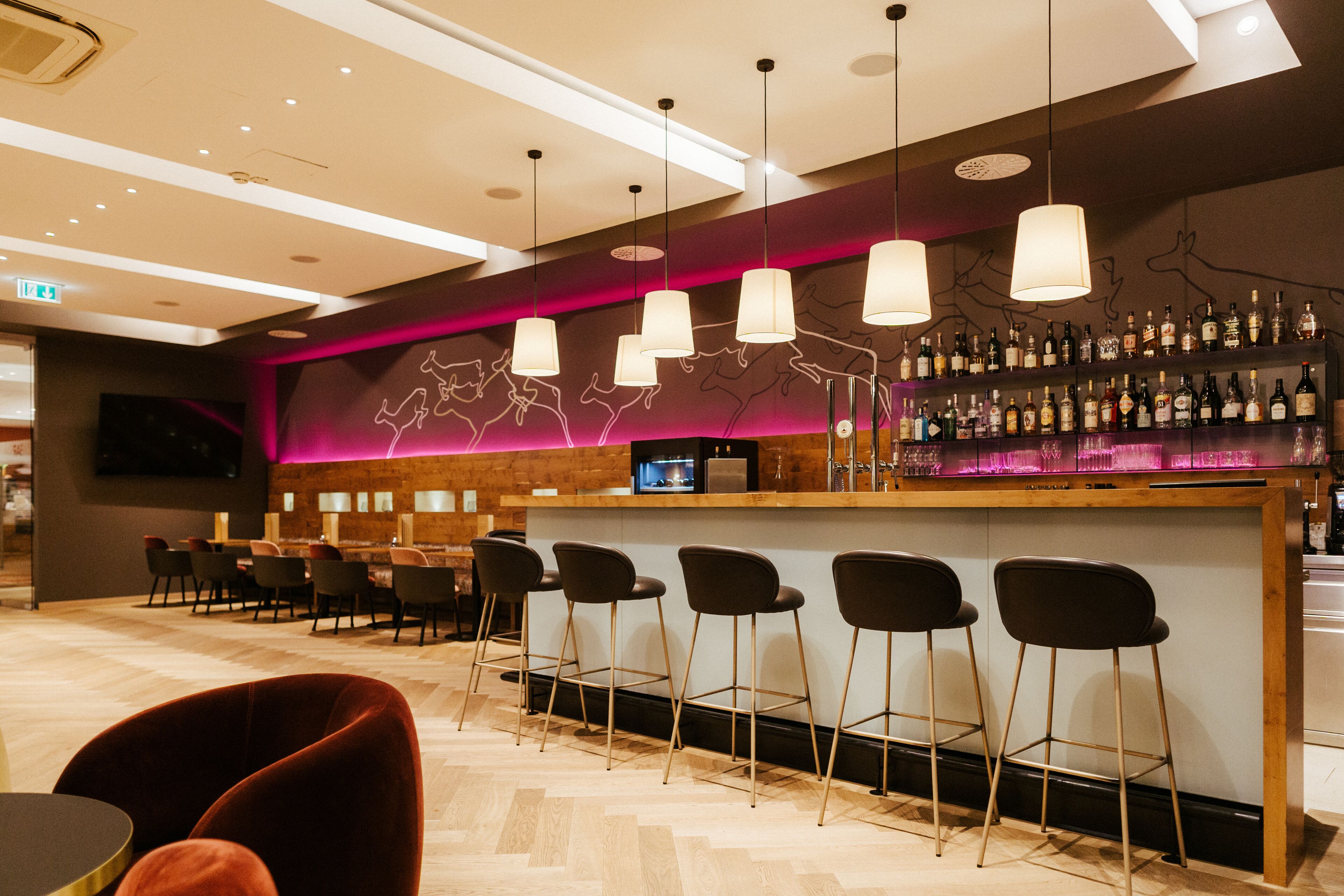 Eine Bar mit einer Holztresen, Barhocker und einem an der Wand montierten Fernseher.
