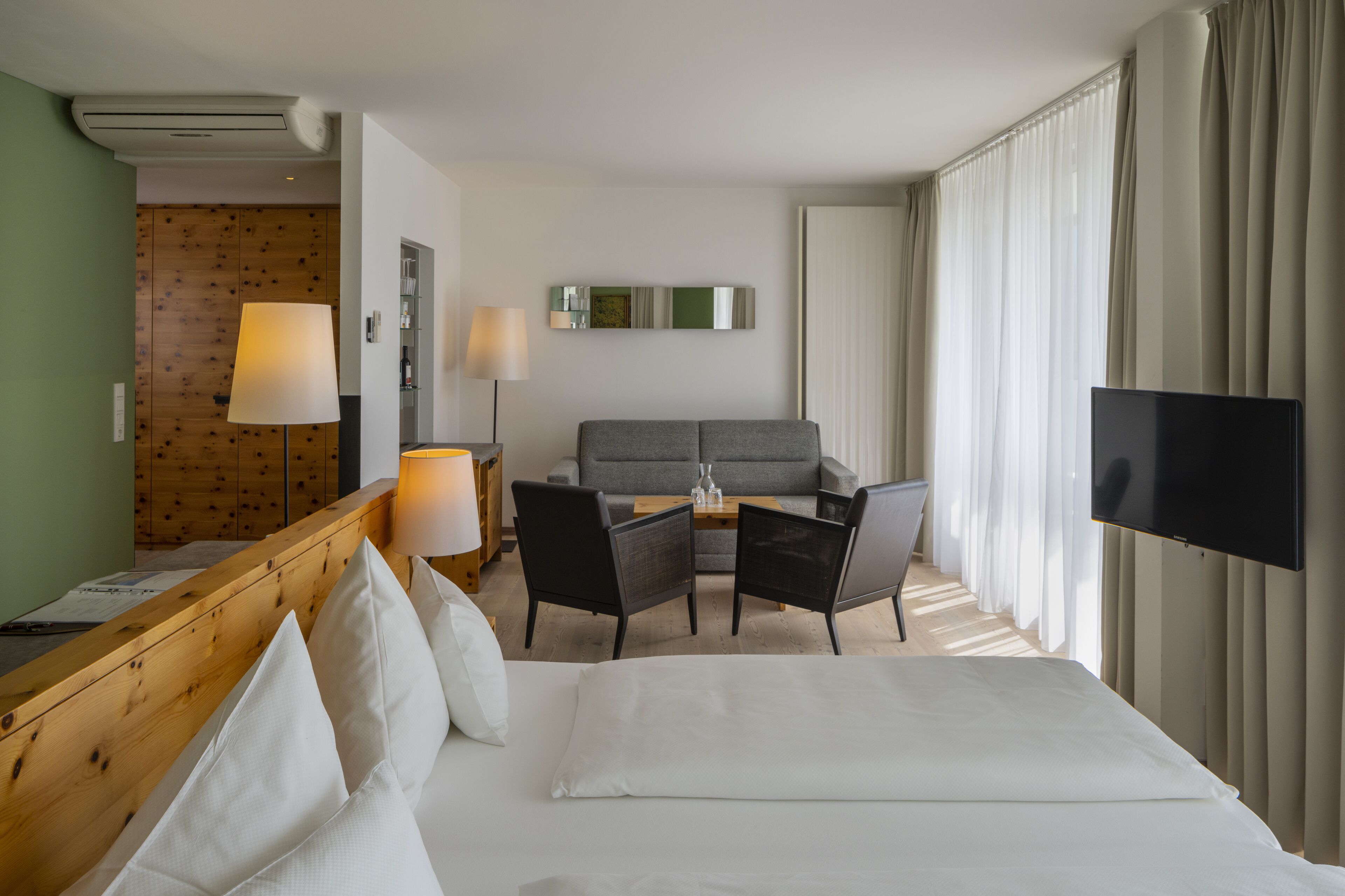 A hotel room with a bed, a desk with a lamp, a sofa, and a TV.