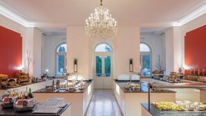 Un hall d’hôtel spacieux, agrémenté d’un magnifique lustre, d’une grande fenêtre en arc de cercle et d’un espace buffet proposant une variété de plats.