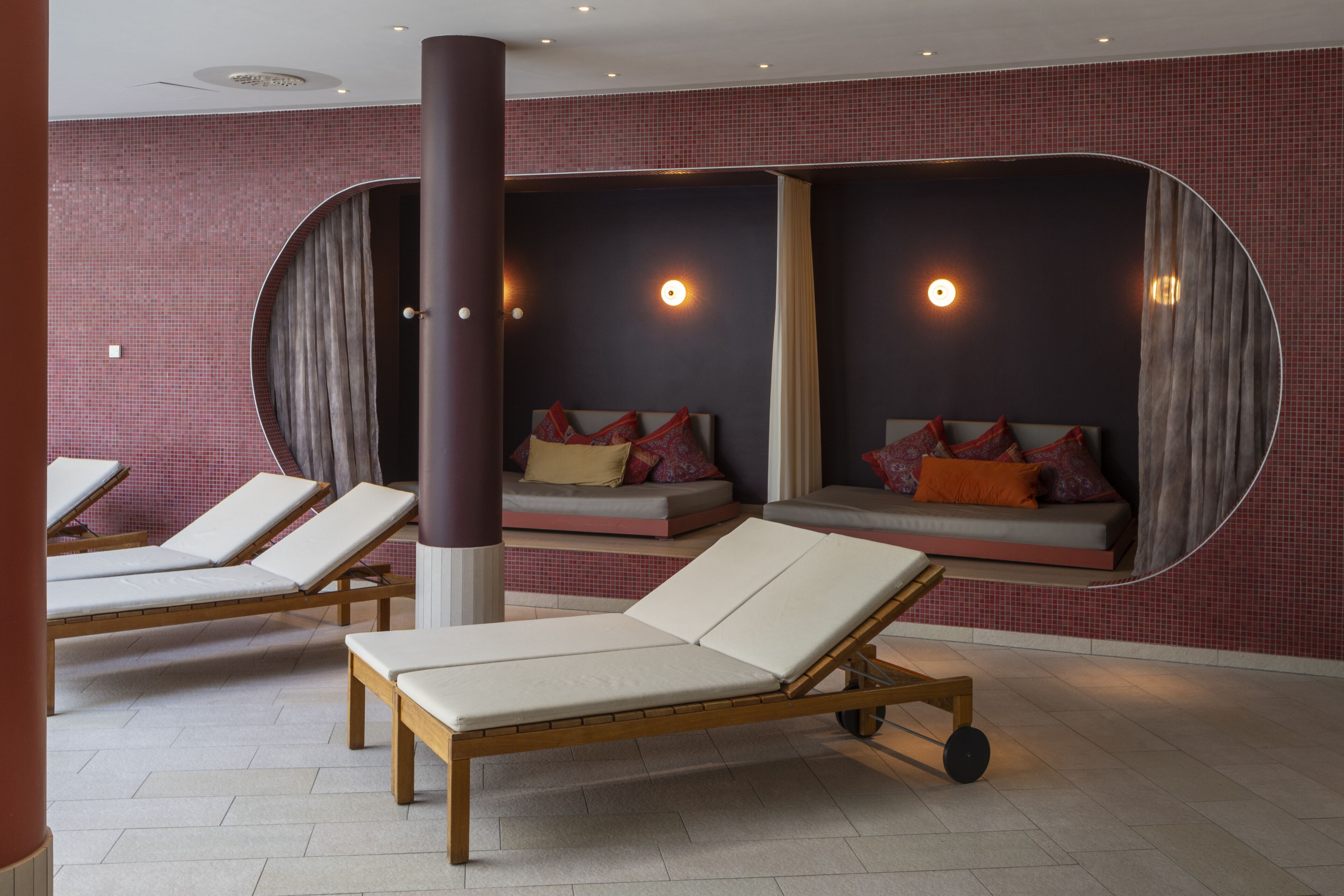 A spa room with two reclining chairs, a massage table, and a wall with a red-tiled pattern.