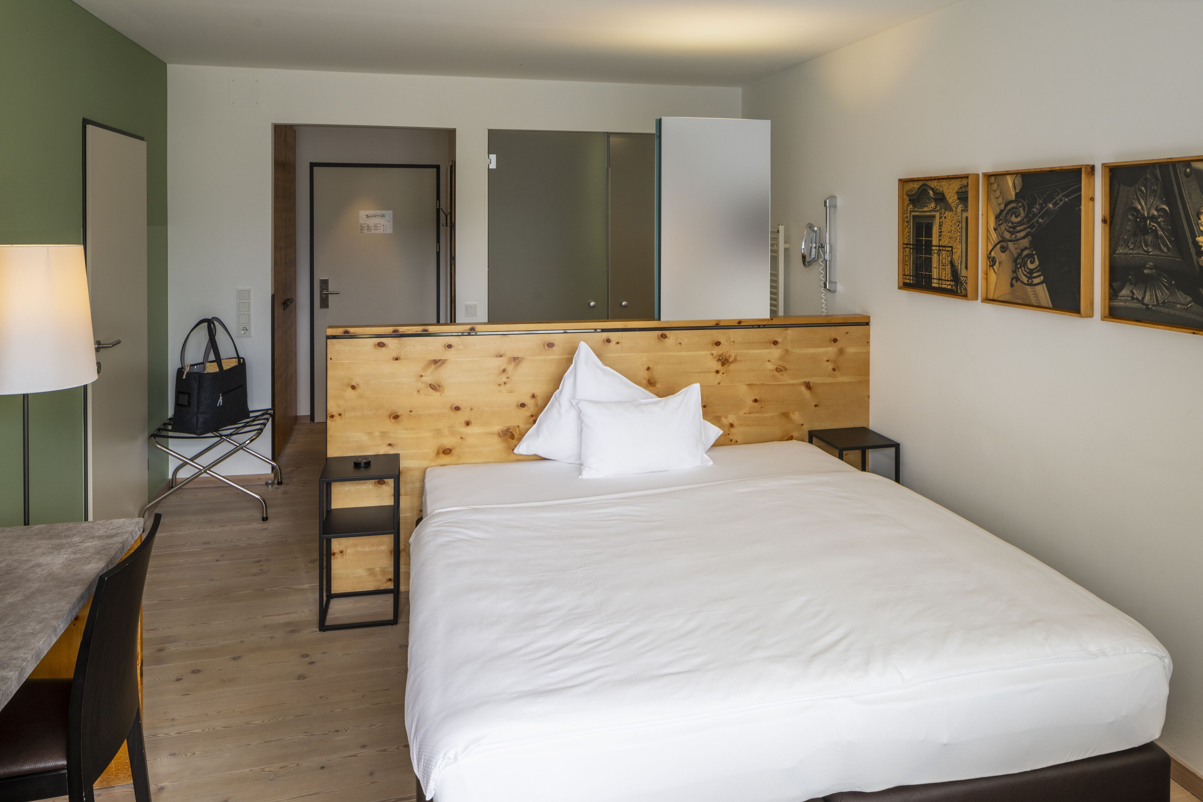 Ein Hotelzimmer mit einem hölzernen Kopfteil, einem Bett mit weißer Bettwäsche, einem Schreibtisch mit Stuhl und einem kleinen Tisch mit Lampe.