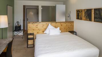 Ein Hotelzimmer mit einem hölzernen Kopfteil, einem Bett mit weißer Bettwäsche, einem Schreibtisch mit Stuhl und einem kleinen Tisch mit Lampe.