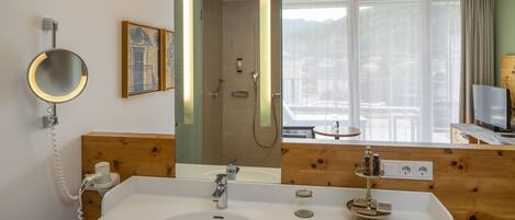 Un baño de hotel con un espejo grande, un lavamanos, una ducha y un televisor.