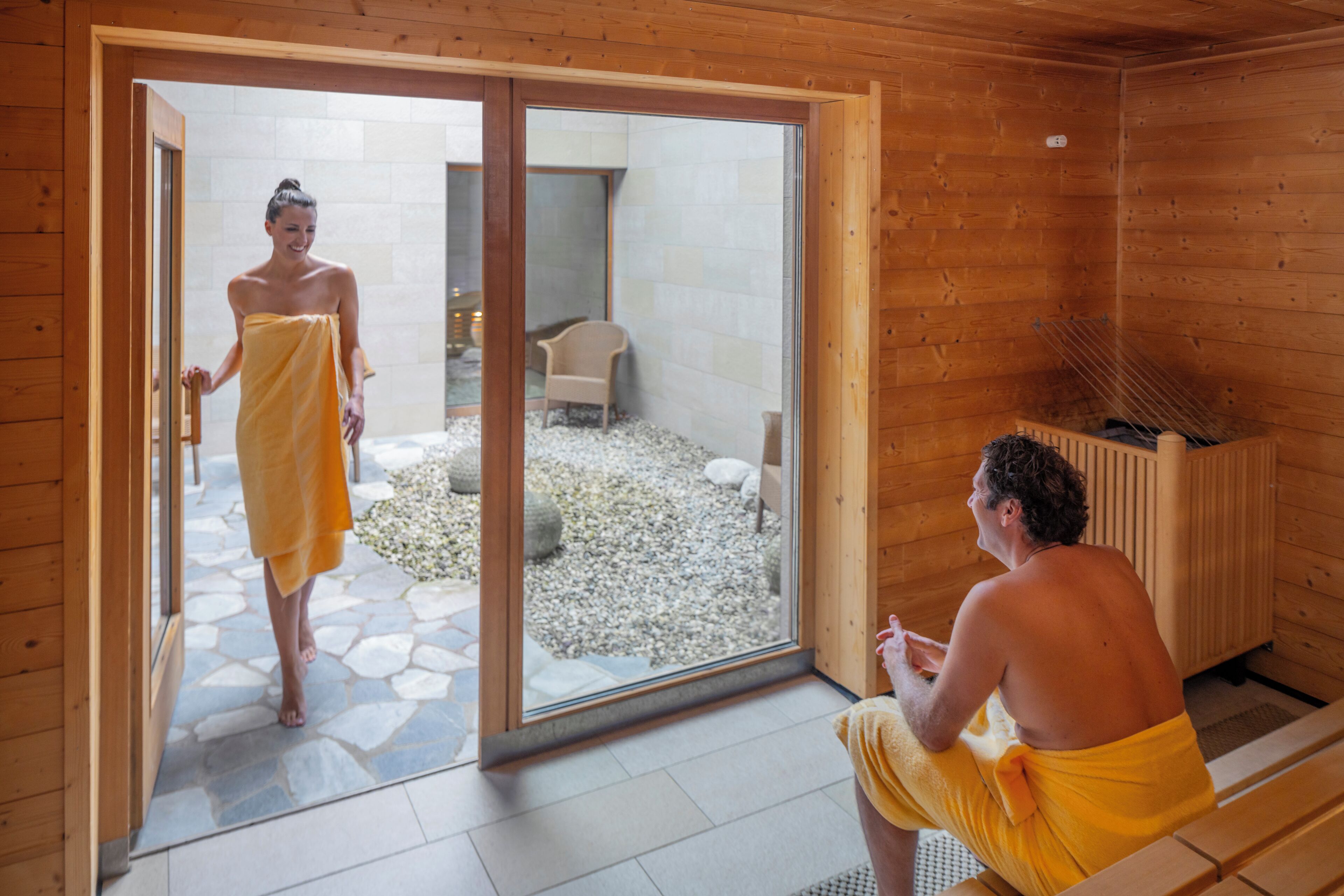 A wooden cabin with a sauna, a stone-tiled floor, and a glass door leading outside.