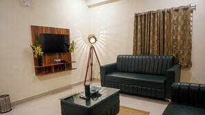 A living room with a sofa, a coffee table, a TV mounted on a wooden panel, and a lamp. - HOTEL URBAN SLEEP (Hyderabad)