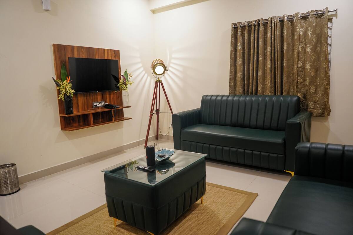 Una sala de estar con un sofá, una mesa de centro, un televisor montado en un panel de madera y una lámpara.