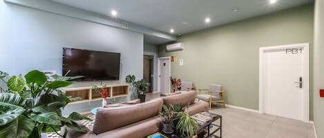 Una sala de estar con televisor de pantalla plana, un sofá, una mesa baja con libros y una estantería.