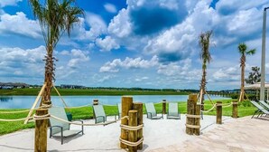 A serene outdoor seating area with lounge chairs and wooden posts, overlooking a calm lake and distant greenery. - "4BR Townhome in Storey Lake, Kissimmee: Private Splash Pool, Resort Amenities!" (Kissimmee)