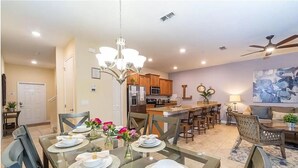 A modern kitchen with a central island, dining area with a glass table set for four, and a living area with a sofa and coffee table. - "4BR Townhome in Storey Lake, Kissimmee: Private Splash Pool, Resort Amenities!" (Kissimmee)