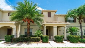 A two-story building with a covered patio area, palm trees, and well-maintained landscaping. - "4BR Townhome in Storey Lake, Kissimmee: Private Splash Pool, Resort Amenities!" (Kissimmee)