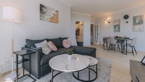Una sala de estar moderna con un sofá gris, una mesa redonda y un comedor con mesa y sillas.
