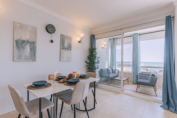 A dining area with a table set for four, a clock, abstract art, and a view of the sea through a balcony. - Sea view gem in Torremolinos REF039 (Torremolinos)