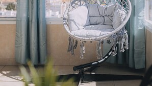 Un balcón con una silla colgante, cortinas y vistas a la ciudad.