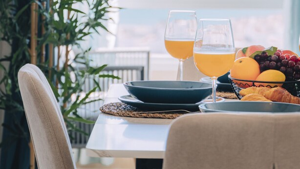 Una mesa de comedor con dos vasos de jugo de naranja, un frutero y un croissant.