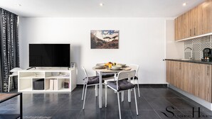 A modern living room with a flat-screen TV, a dining table with chairs, a bookshelf, and a kitchen area with wooden cabinets. - Stylish Seaview Terrace Retreat  REF002 (Torremolinos)