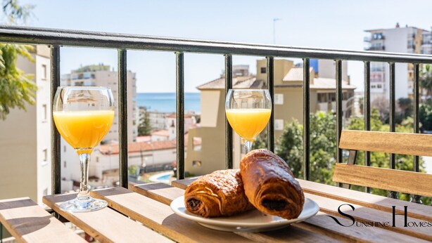 A balcony with a wooden table, two glasses of orange juice, and two croissants on a plate. - Stylish Seaview Terrace Retreat  REF002 (Torremolinos)