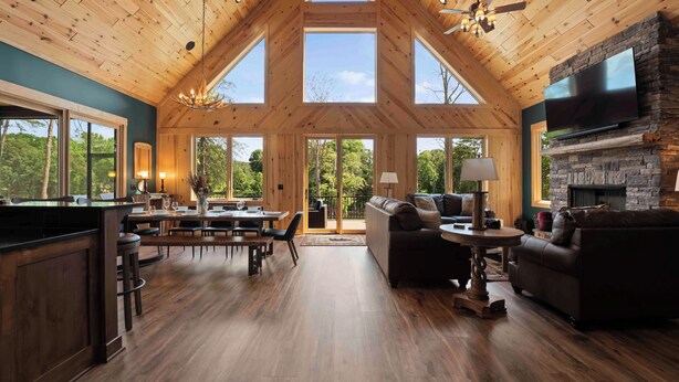 A spacious interior with a high wooden ceiling, a stone fireplace, and large windows offering views of the outdoors.