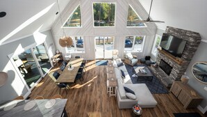 A spacious living area with a stone fireplace, large windows, and a high ceiling. - Luxe Lakefront Lodge w/ Pool, Hot Tub, Theater & Private Dock | Sleeps 21 (Sherrills Ford)