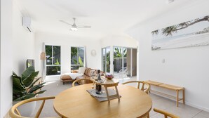 A spacious dining area with a round wooden table, chairs, and a bench. There is a ceiling fan, large windows, and a view of the outdoors. - 600m to esplanade - Spacious + Everything you need (Pialba)