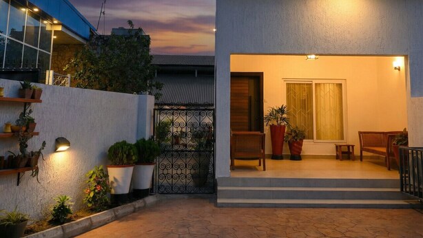 A modern building with a flat roof, a balcony, and a door leading to an interior space with a bench and potted plants.