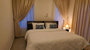 A hotel room with a large bed, beige curtains, a bedside lamp, and a nightstand.