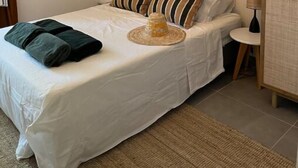 Ein ordentlich bezogenes Bett mit gestreiften Kissen, einem gewebten Korb und aufgerollten Handtüchern.