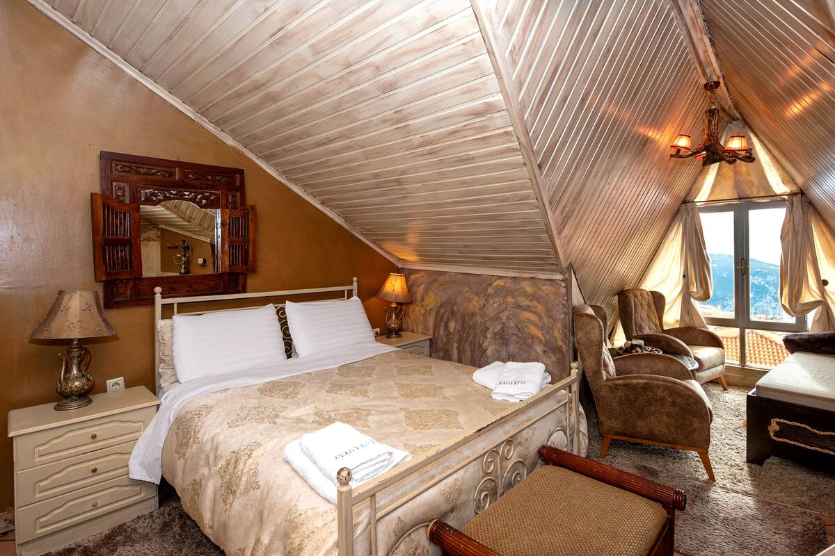 Une chambre à coucher avec un lit, une chaise, un bureau, une lampe et une fenêtre avec des rideaux.