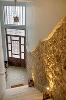 Una escalera con pared de piedra texturizada, una reja metálica decorativa y un candelabro colgante.