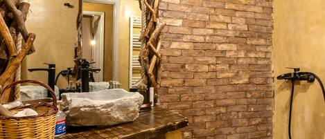 A rustic bathroom with a stone sink, wooden beams, and a stone bathtub.