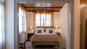 Ein Schlafzimmer mit einem großen Bett, Holzboden, zwei Nachttischlampen und Blick ins Freie durch transparente Vorhänge.