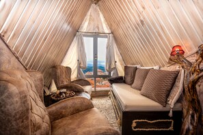Une pièce confortable, de forme triangulaire et aménagée comme une tente, avec un lit, deux canapés et une petite table.
