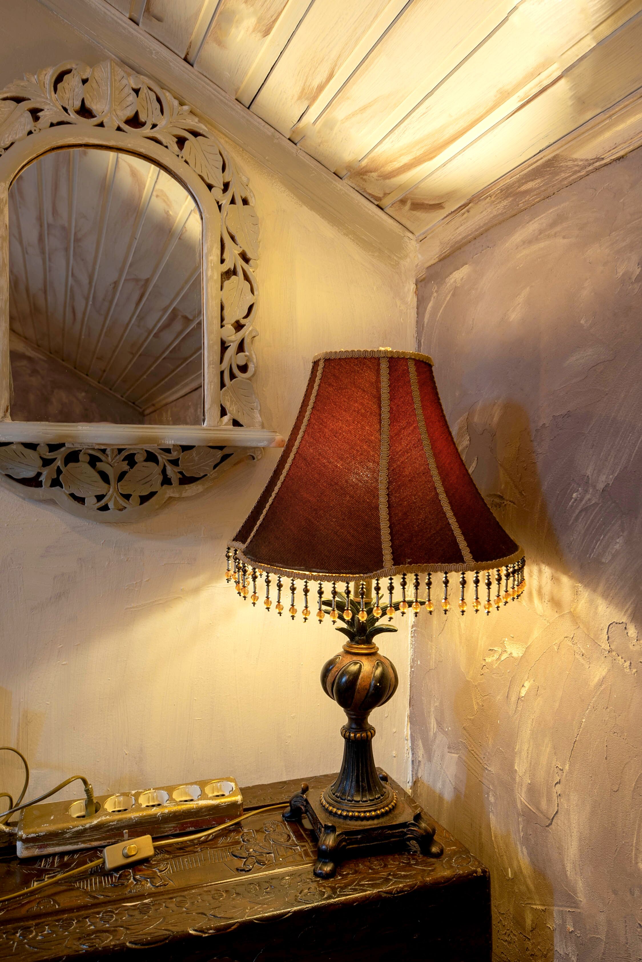 A lamp with a red shade and decorative trim on a wooden table.