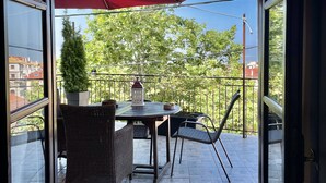 Ein offener Balkon mit Tisch, Stühlen, einer Topfpflanze und einem roten Sonnenschirm.