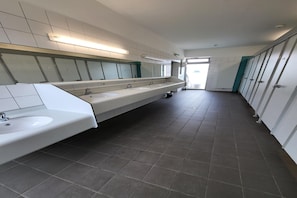 Des toilettes modernes avec trois lavabos, un grand miroir et un sol carrelé.